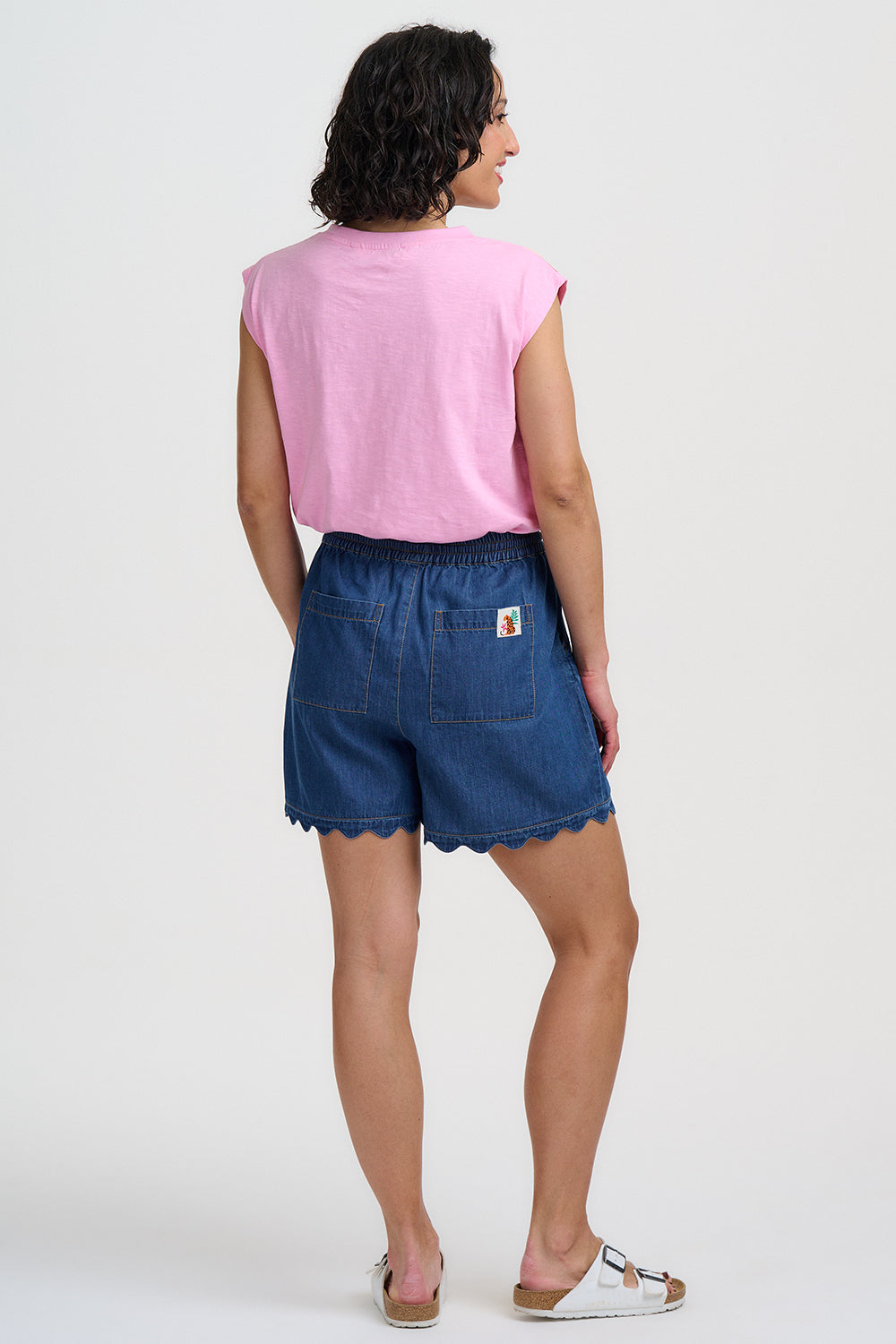 Person wearing a pink sleeveless top and blue shorts on a white background