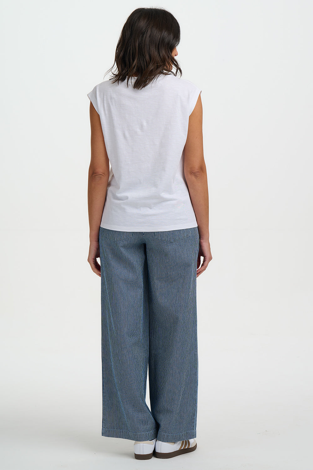 Person wearing a white sleeveless top and blue pants on a white background