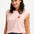 A woman smiling and wearing a pink sleeveless T-shirt with a rainbow parrot embroidery on the chest pocket, paired with blue jeans.