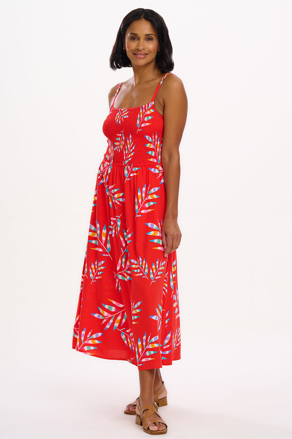 A model wearing a red midi dress with a tropical leaf print and a shirred bust, sleeveless.