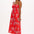A model wearing a red midi dress with a tropical leaf print and a shirred bust, sleeveless.