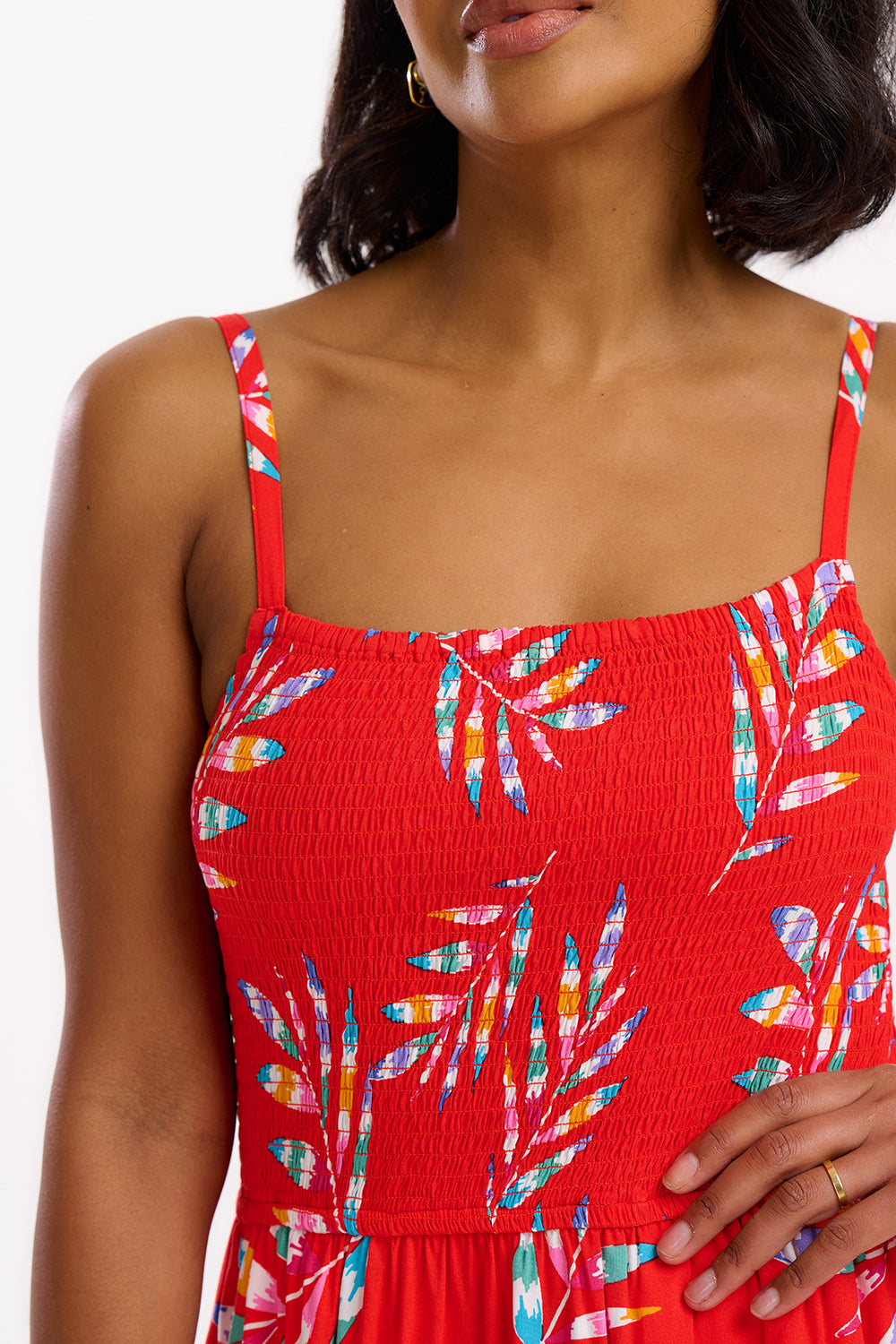 A model wearing a red midi dress with a tropical leaf print and a shirred bust, sleeveless.