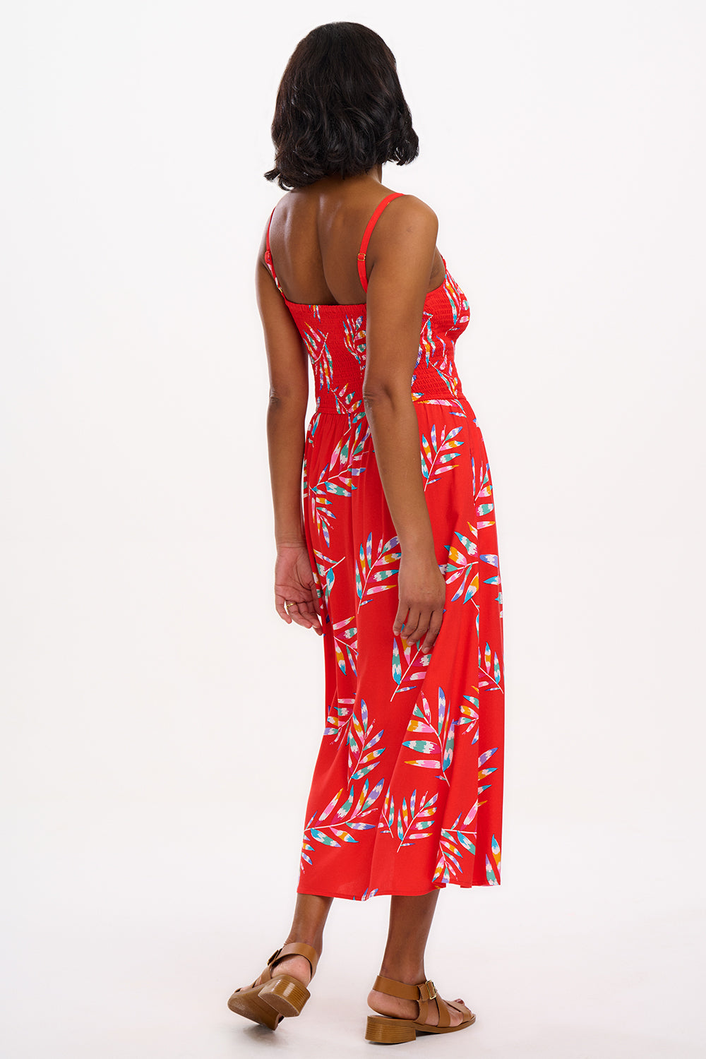 A model wearing a red midi dress with a tropical leaf print and a shirred bust, sleeveless.