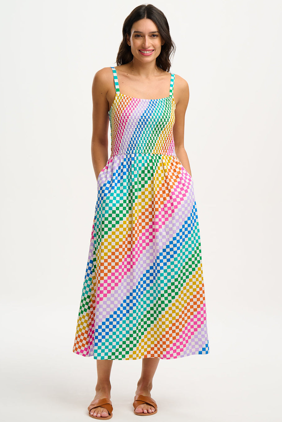 A woman wearing a multicolored rainbow checkerboard sundress with shirred top and midi length.