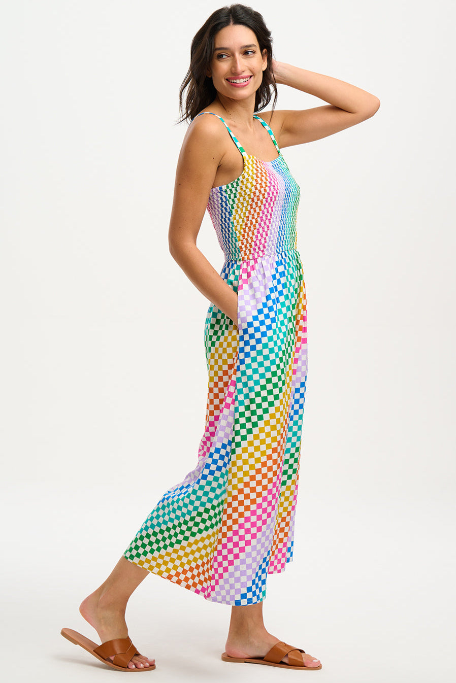 A woman wearing a multicolored rainbow checkerboard sundress with shirred top and midi length.