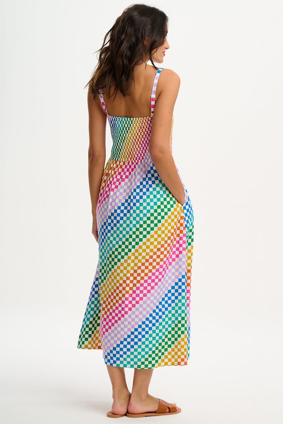A woman wearing a multicolored rainbow checkerboard sundress with shirred top and midi length.
