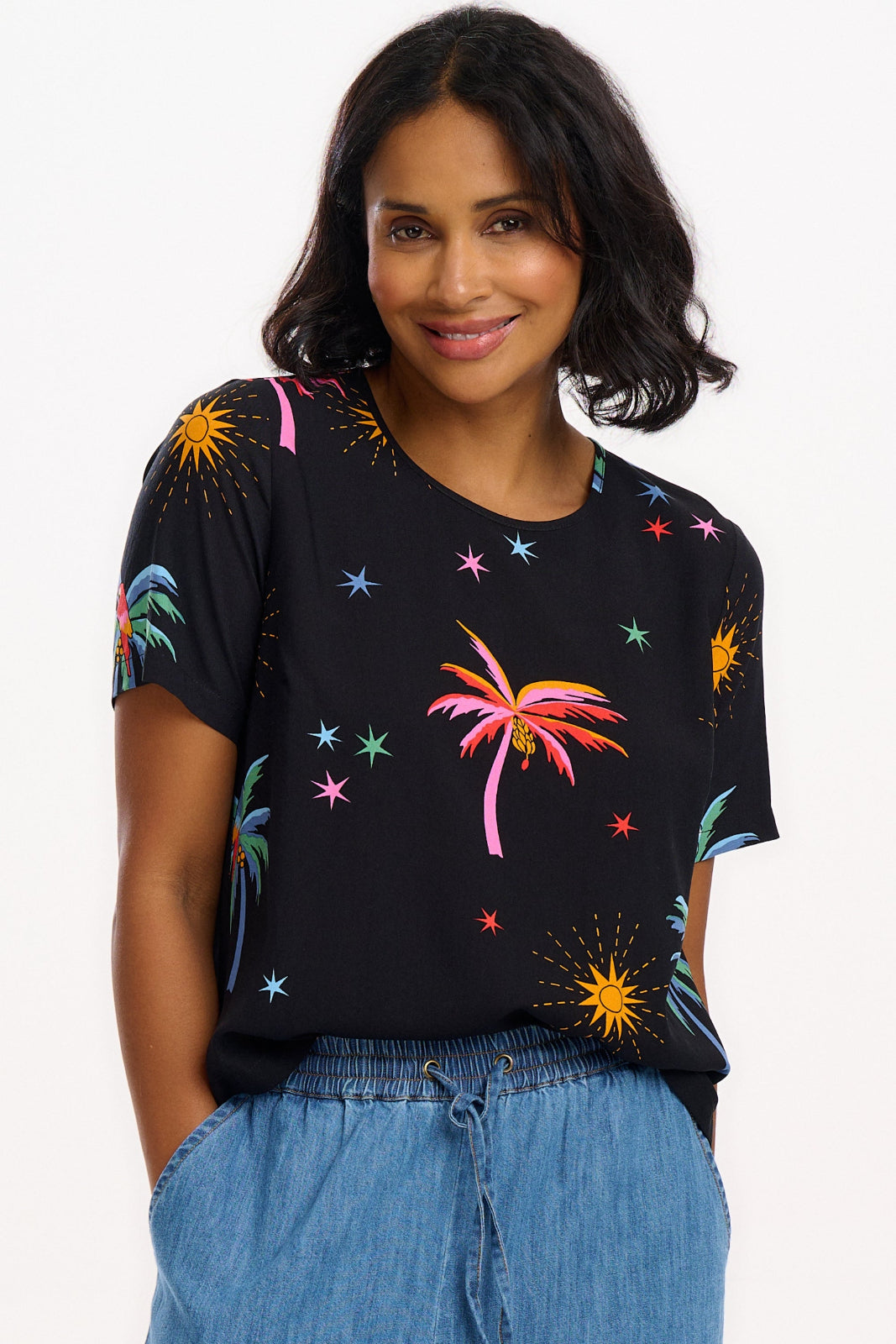 A woman wearing a black t-shirt with a colorful palm tree and star pattern, paired with blue denim jeans.