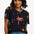 A woman wearing a black t-shirt with a colorful palm tree and star pattern, paired with blue denim jeans.