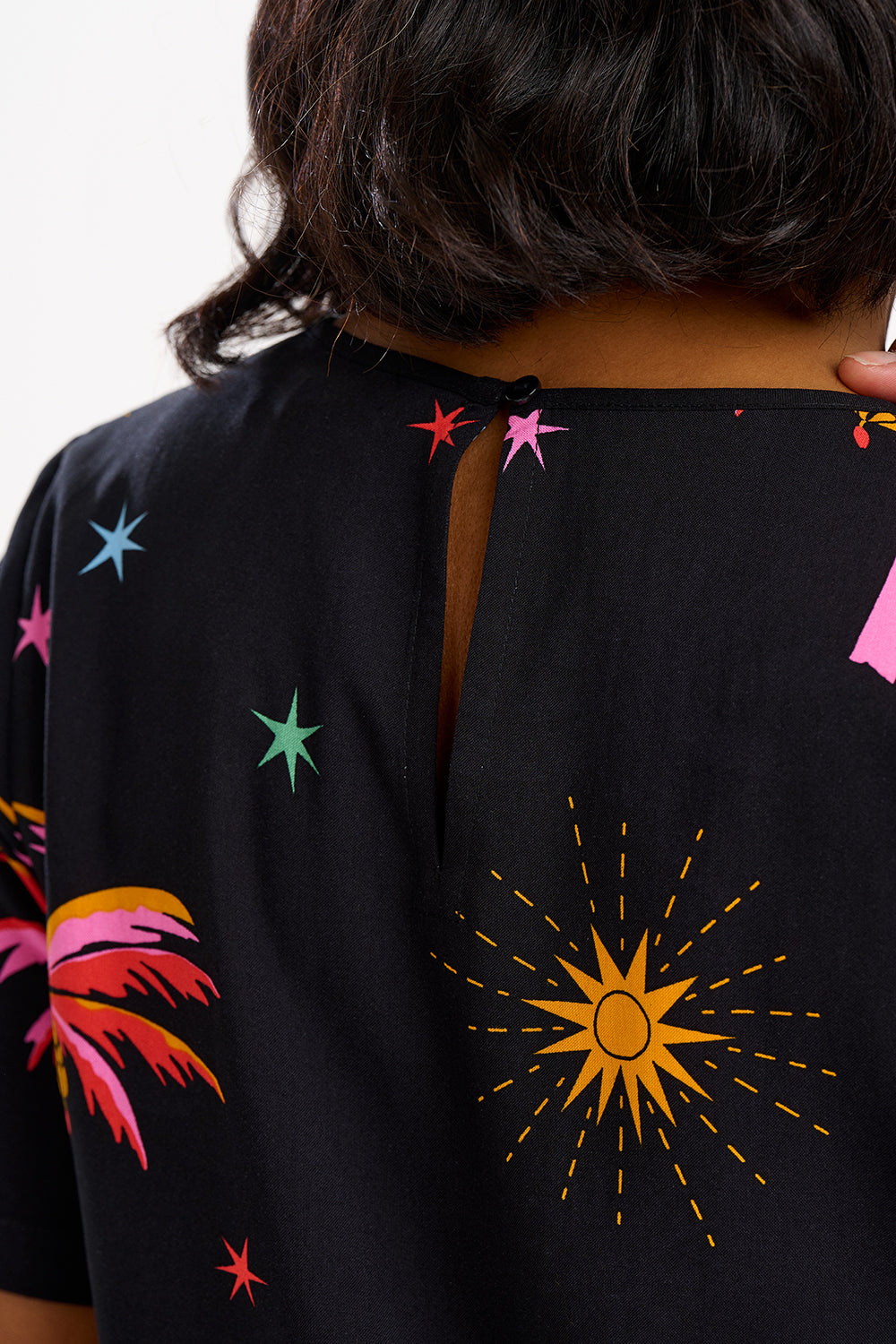 A woman wearing a black t-shirt with a colorful palm tree and star pattern, paired with blue denim jeans.