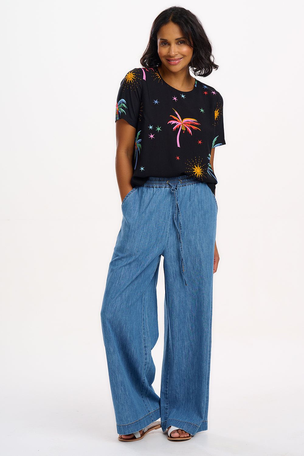 A woman wearing a black t-shirt with a colorful palm tree and star pattern, paired with blue denim jeans.
