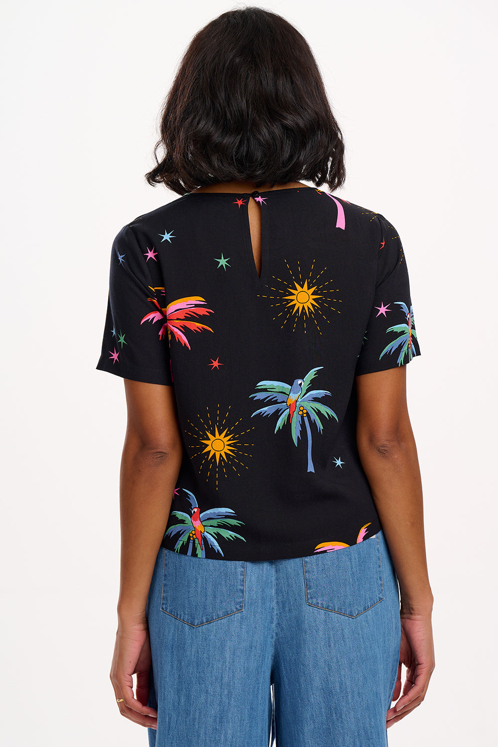 A woman wearing a black t-shirt with a colorful palm tree and star pattern, paired with blue denim jeans.