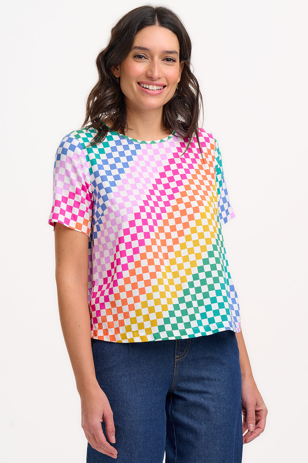 A woman smiling and wearing a multicolored rainbow checkerboard patterned t-shirt with a crew neckline and short sleeves.
