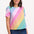 A woman smiling and wearing a multicolored rainbow checkerboard patterned t-shirt with a crew neckline and short sleeves.