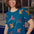 A woman smiling and wearing a teal t-shirt with a pattern of colorful rainbow parrots.