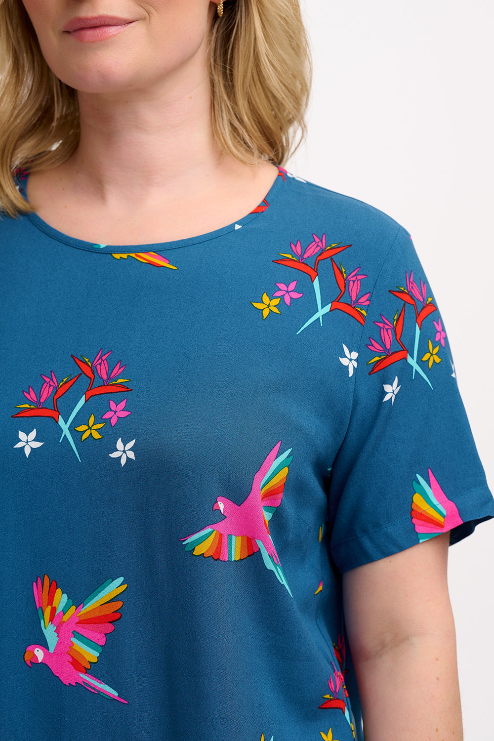 A woman wearing a teal t-shirt with a pattern of rainbow parrots, paired with jeans.