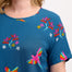 A woman wearing a teal t-shirt with a pattern of rainbow parrots, paired with jeans.