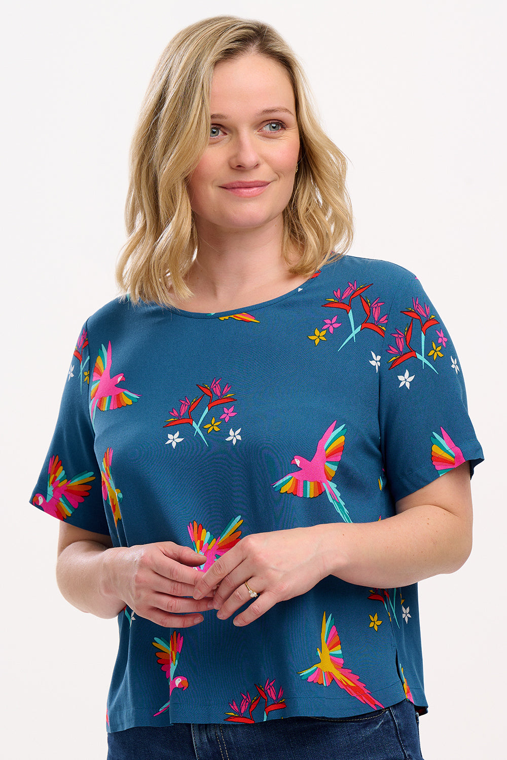 A woman wearing a teal t-shirt with a pattern of rainbow parrots, paired with jeans.