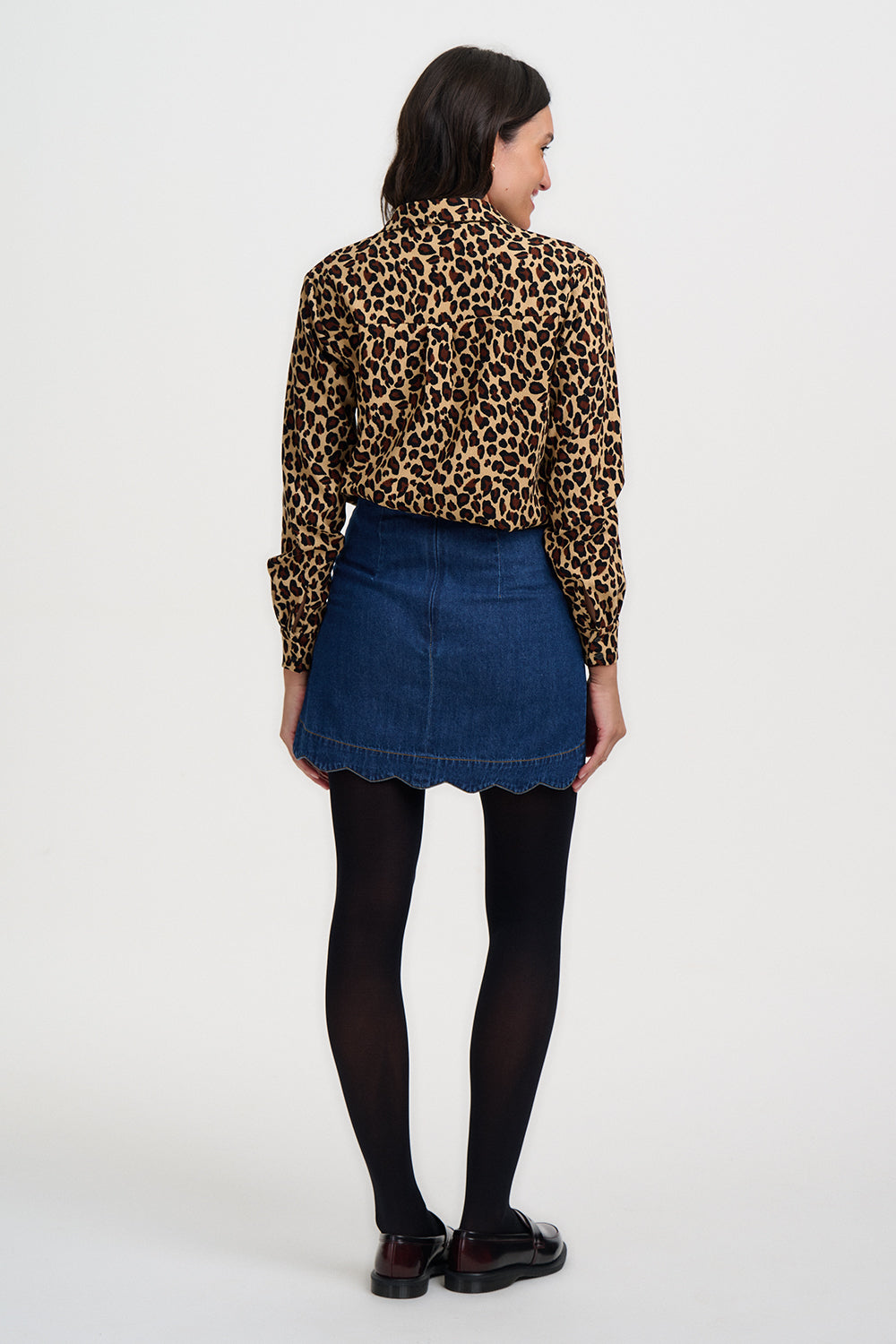 Person wearing a leopard print shirt, blue denim skirt, and black tights on a white background