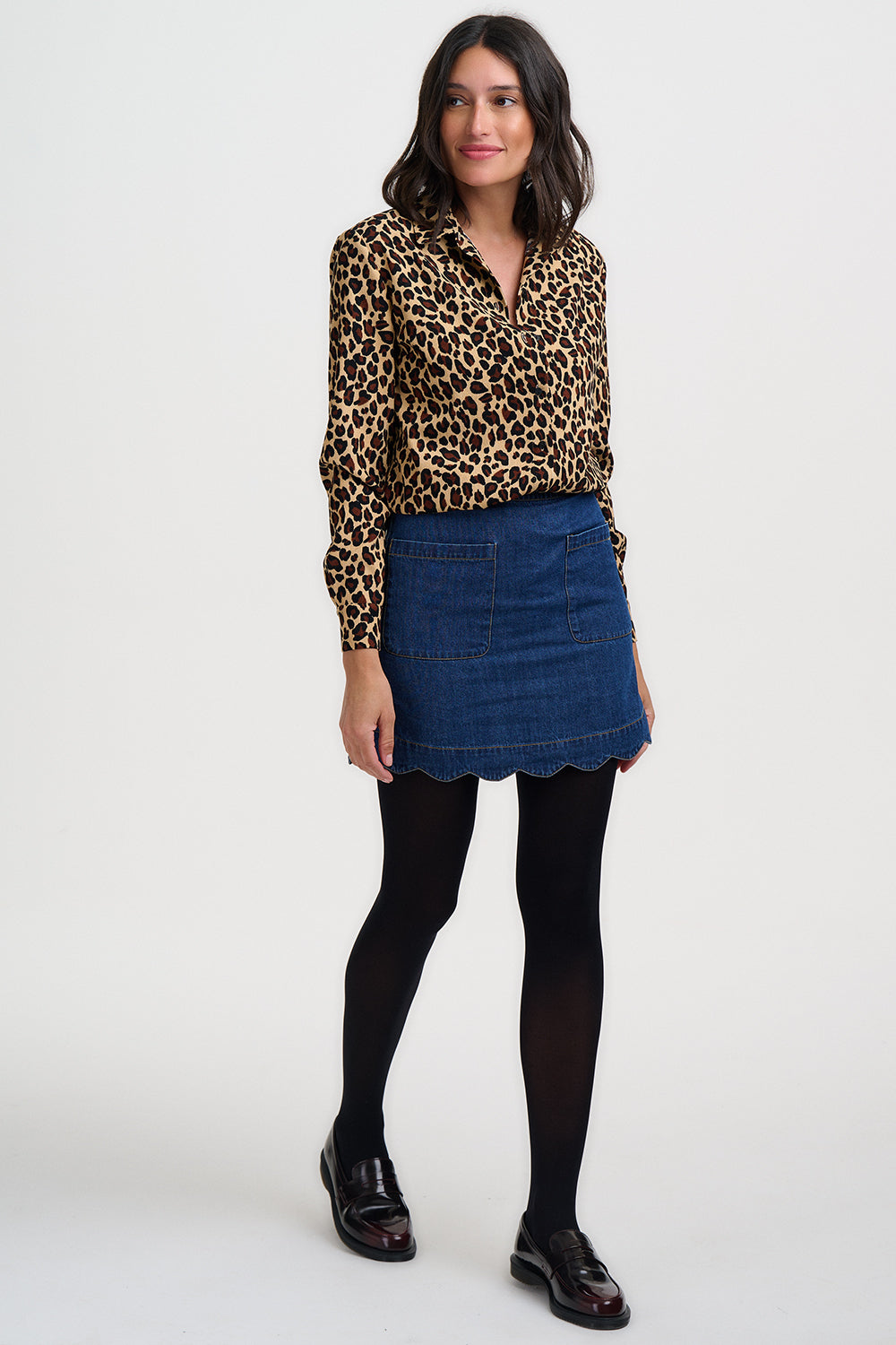Woman wearing a leopard print blouse, blue denim skirt, and black tights on a white background