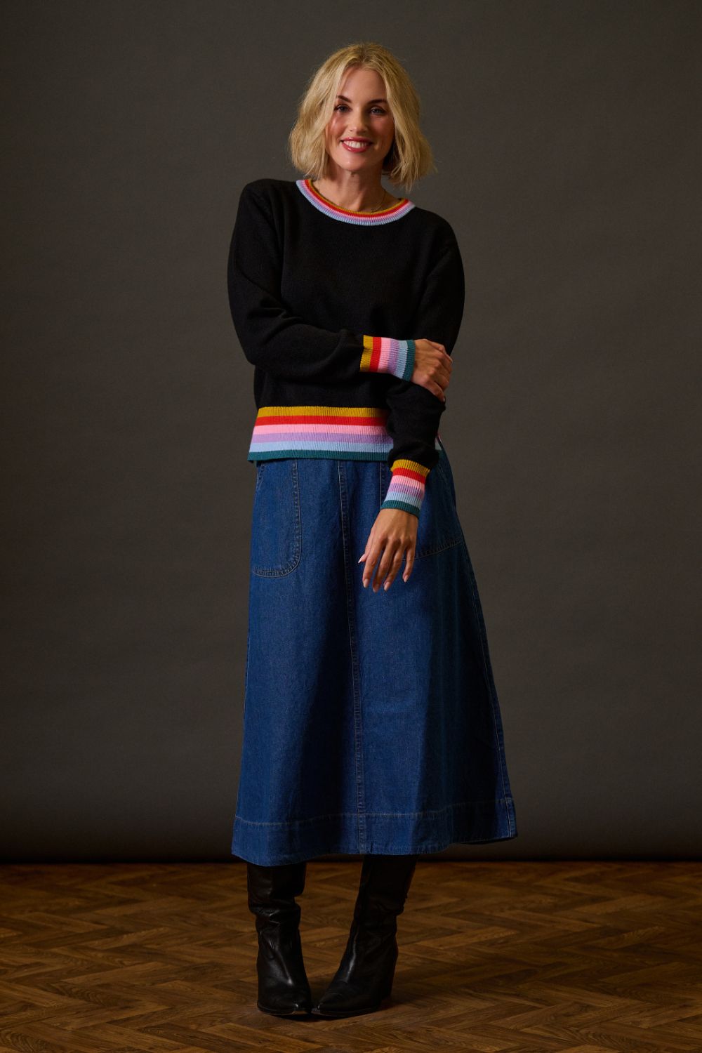 Woman wearing a black sweater with colorful stripes and a blue skirt against a dark background