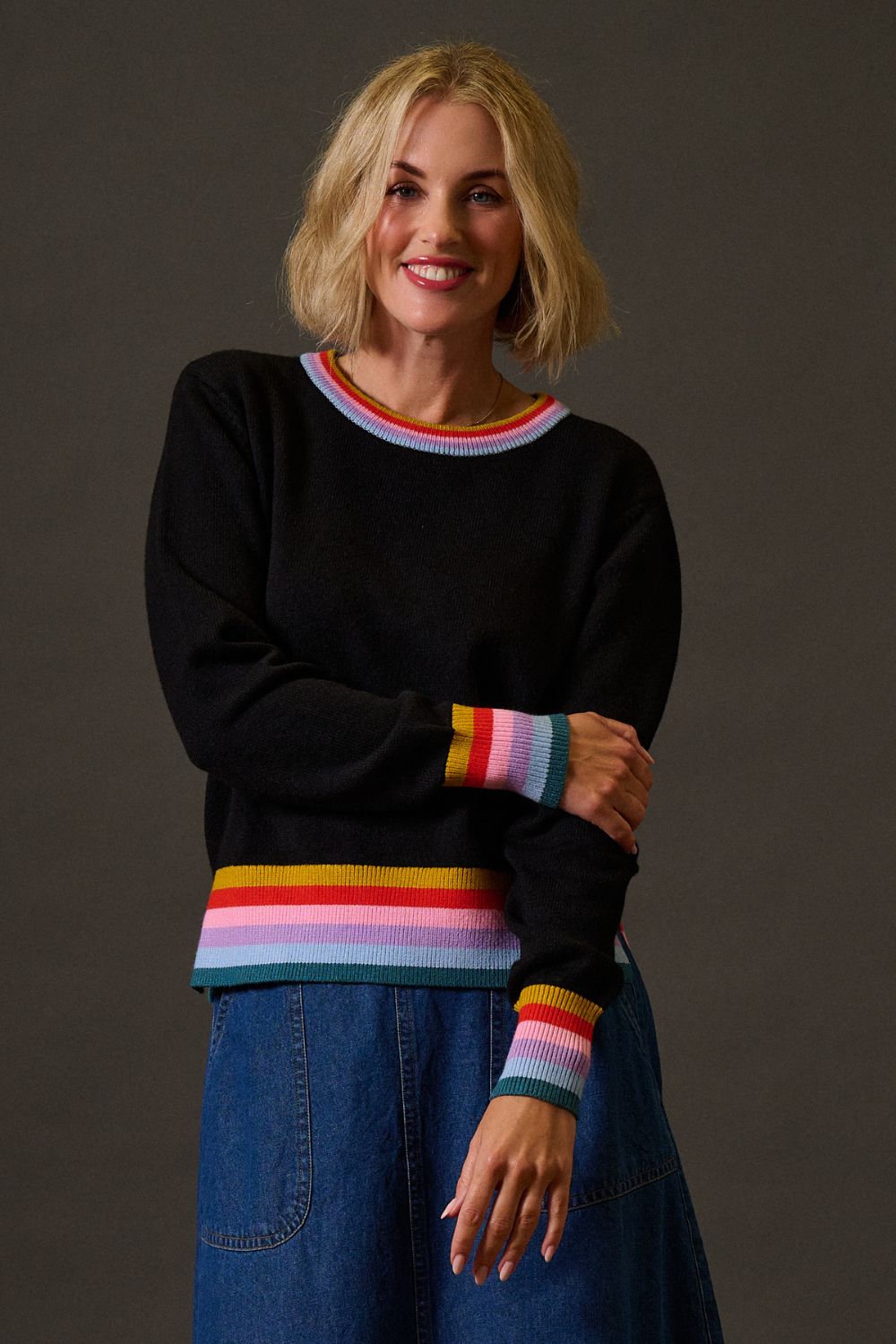Woman wearing a black sweater with colorful stripes on a dark background