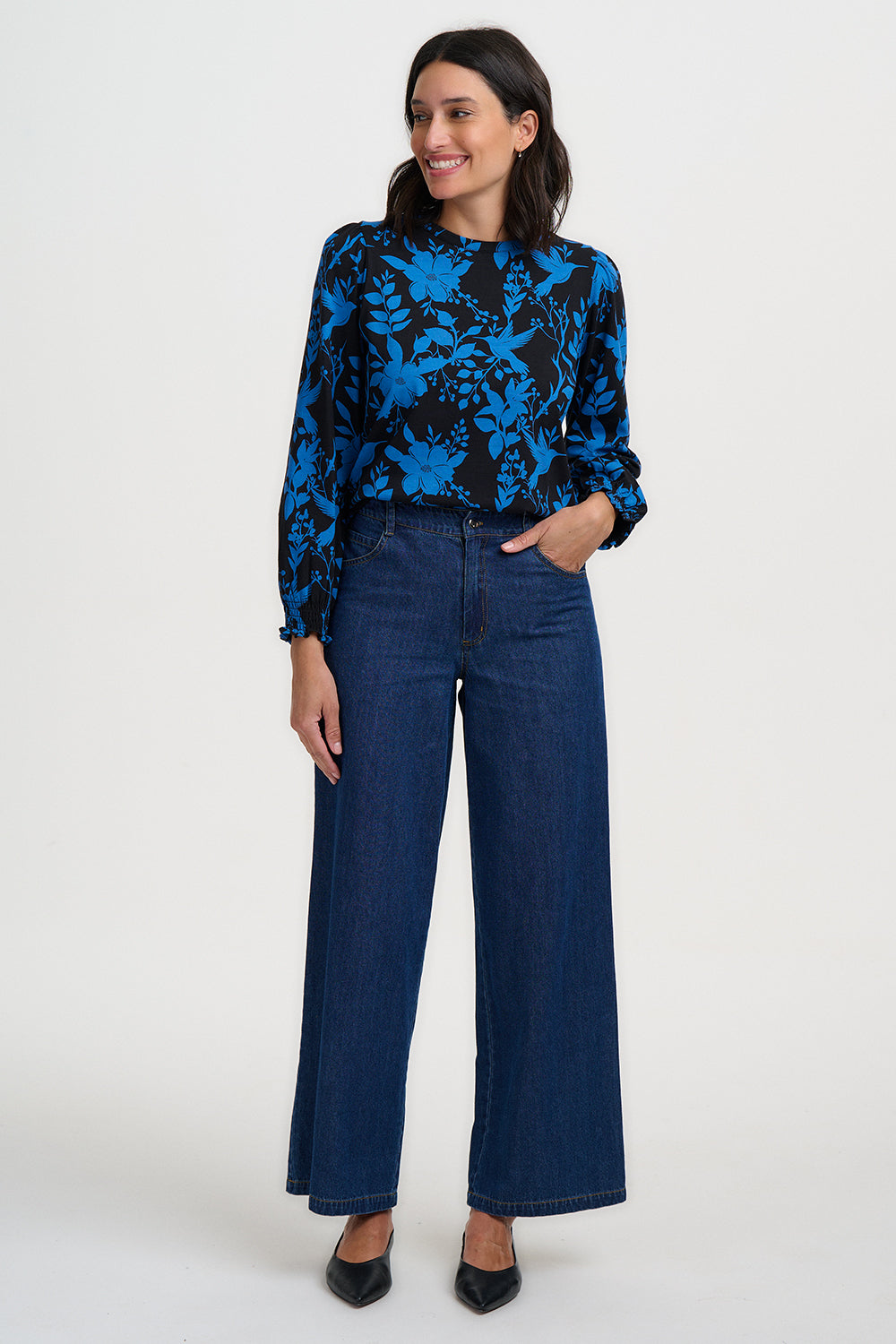 Woman wearing a blue and black patterned blouse with wide-leg jeans on a white background