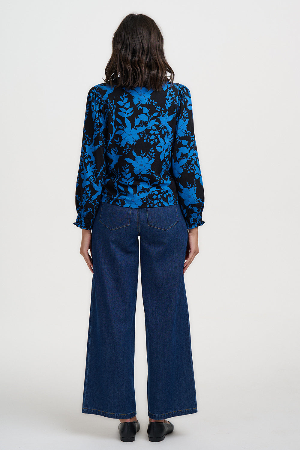 Person wearing a blue floral blouse and dark jeans on a white background