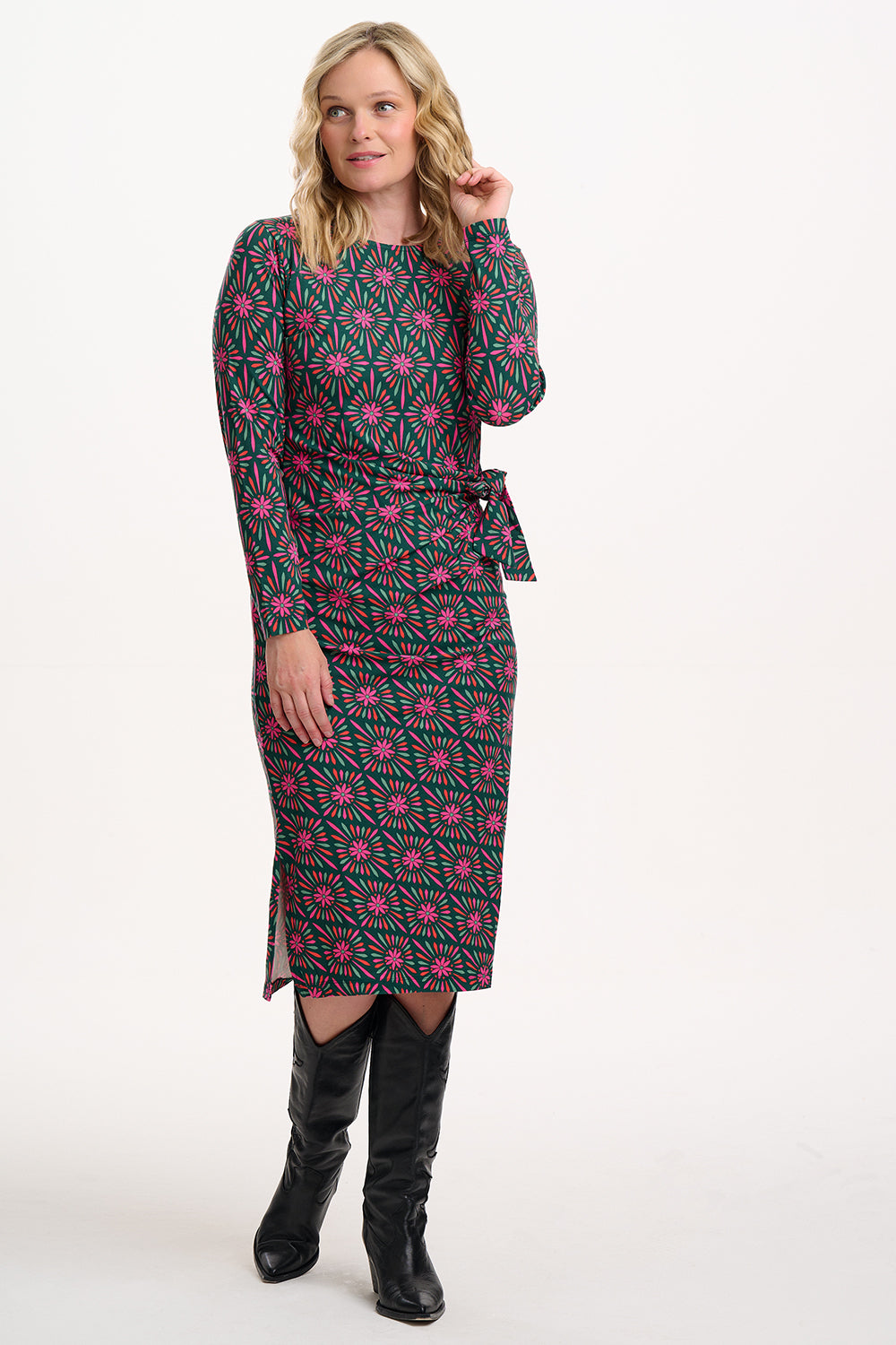 Sugarhill brighton model wearing a patterned dress with a belt and black boots on a white background