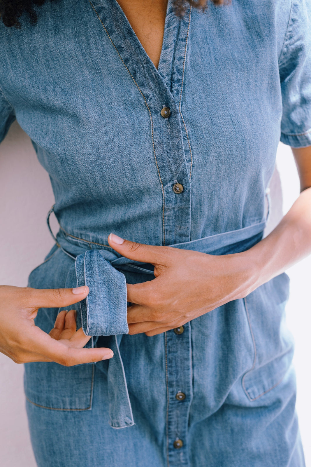 Person wearing a blue denim dress with a belt against a light background