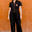 Woman wearing a black jumpsuit with a red heart design against an orange wall.