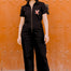 Woman wearing a black jumpsuit with a red heart design against an orange wall.