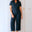Woman wearing a dark blue jumpsuit standing against a white wall.