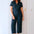 Woman wearing a dark blue jumpsuit standing against a white wall.