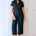 Woman wearing a dark blue jumpsuit standing against a white wall.