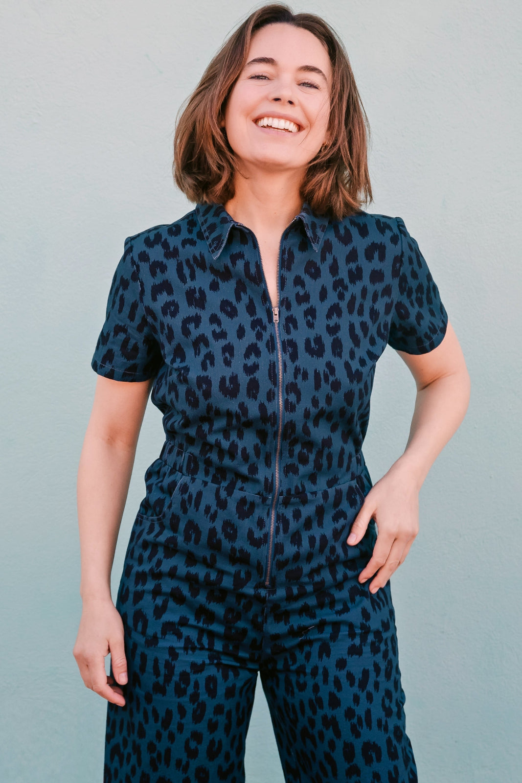 A woman smiling and posing in a navy jumpsuit with a black leopard print pattern, featuring short sleeves and wide flared legs.