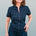 A woman smiling and posing in a navy jumpsuit with a black leopard print pattern, featuring short sleeves and wide flared legs.