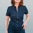 A woman smiling and posing in a navy jumpsuit with a black leopard print pattern, featuring short sleeves and wide flared legs.
