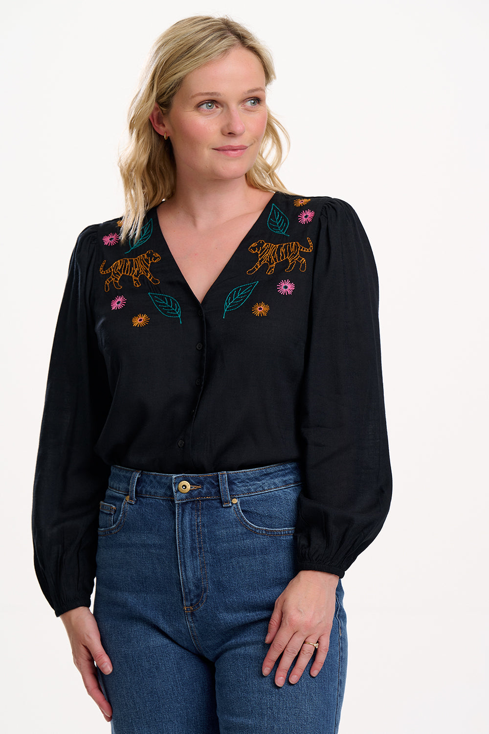 Woman wearing a black blouse with colorful embroidery and blue jeans on a white background