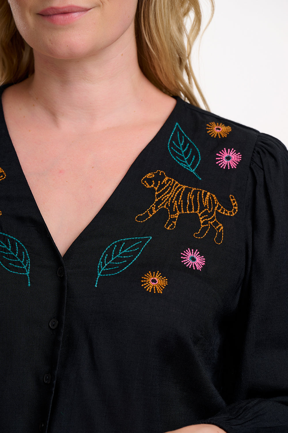 Black blouse with colorful embroidery of a tiger and leaves worn by a person.