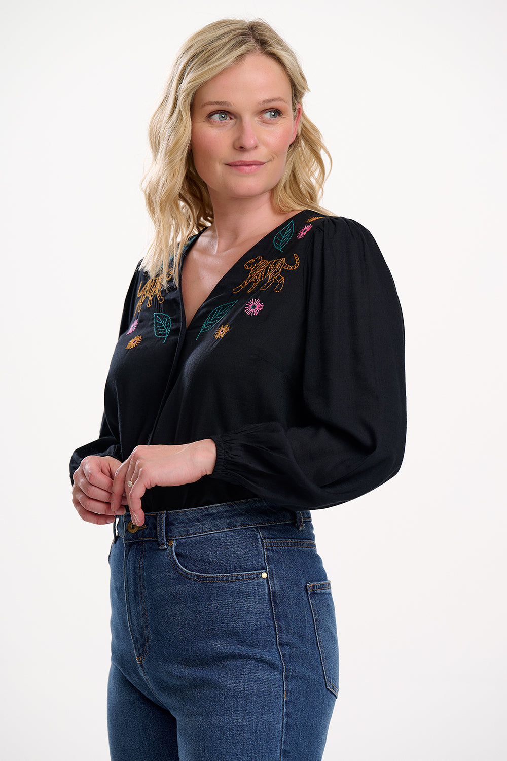 Woman wearing a black blouse with floral embroidery and blue jeans on a white background