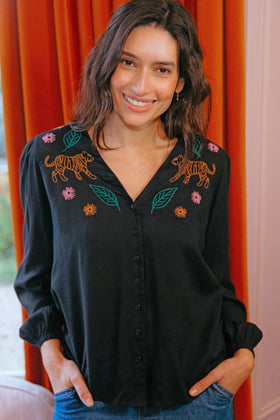 Woman wearing a black blouse with tiger and floral embroidery against an orange curtain background