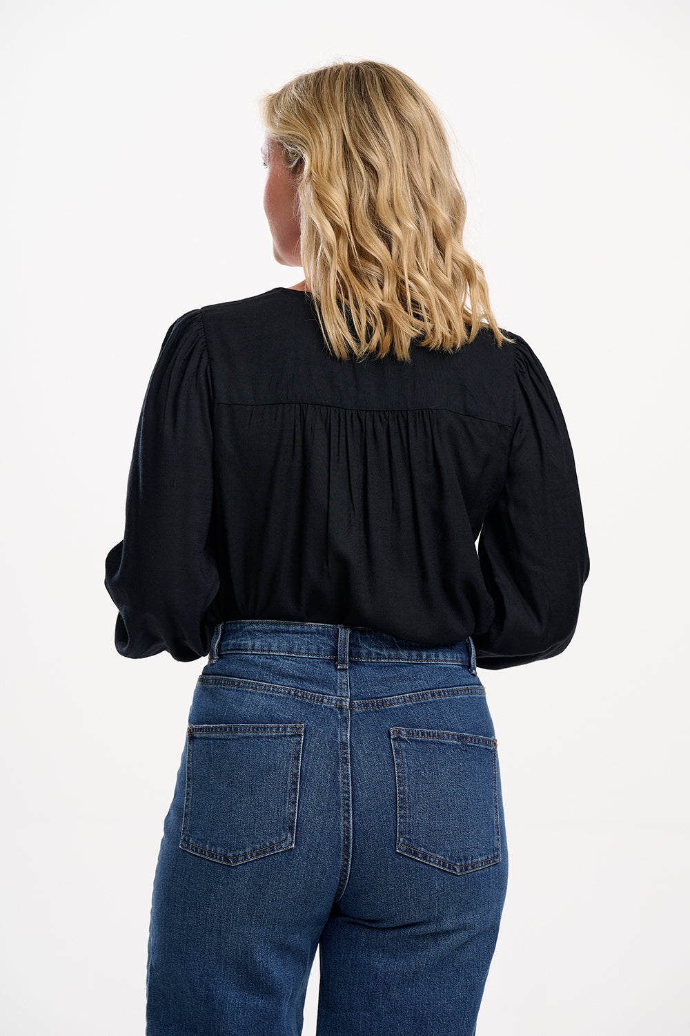 Person wearing a black blouse and blue jeans on a white background