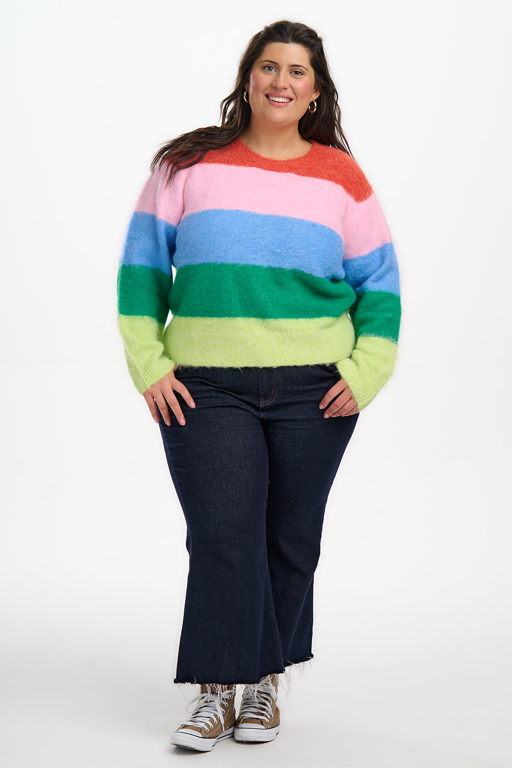 Person wearing a colorful striped sweater and dark jeans on a white background