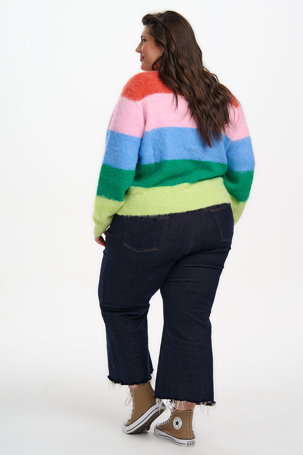 Person wearing a colorful striped sweater and dark pants on a white background