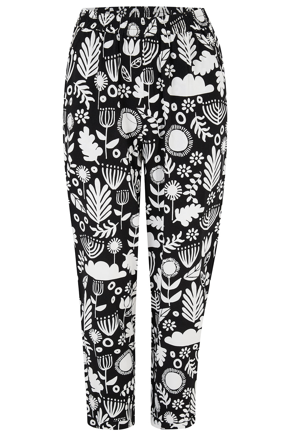 A woman standing, wearing a black top and Debbs trousers with a monochrome floral pattern.
