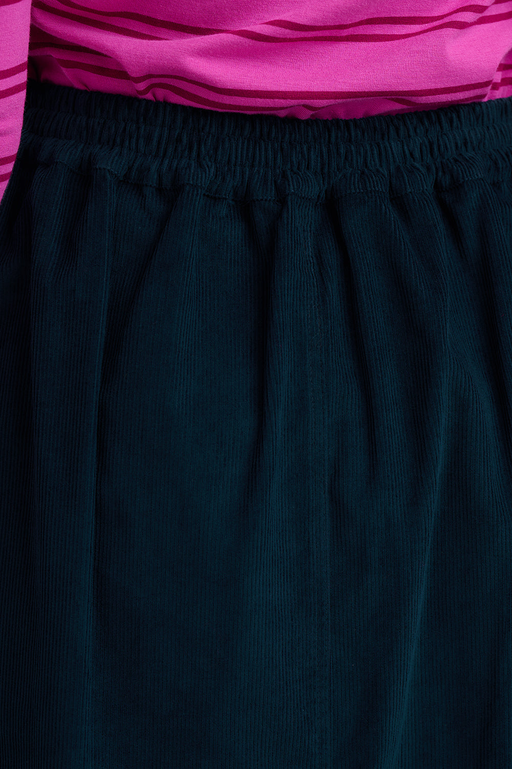 Close-up of a person wearing dark navy corduroy pants with an elastic waistband, paired with a bright pink striped top.