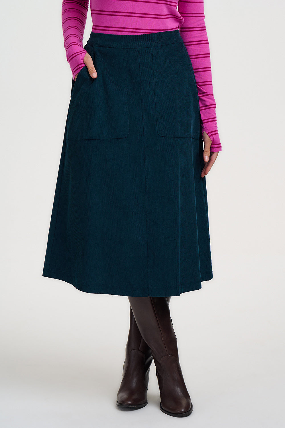 Person wearing a navy blue skirt with a pink top and brown boots on a white background