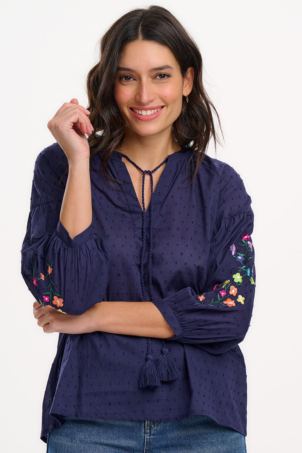 A woman wearing a navy blue boho top with embroidered flowers on the sleeves, featuring a deep V-neck with tassel ties and 3/4 length sleeves.