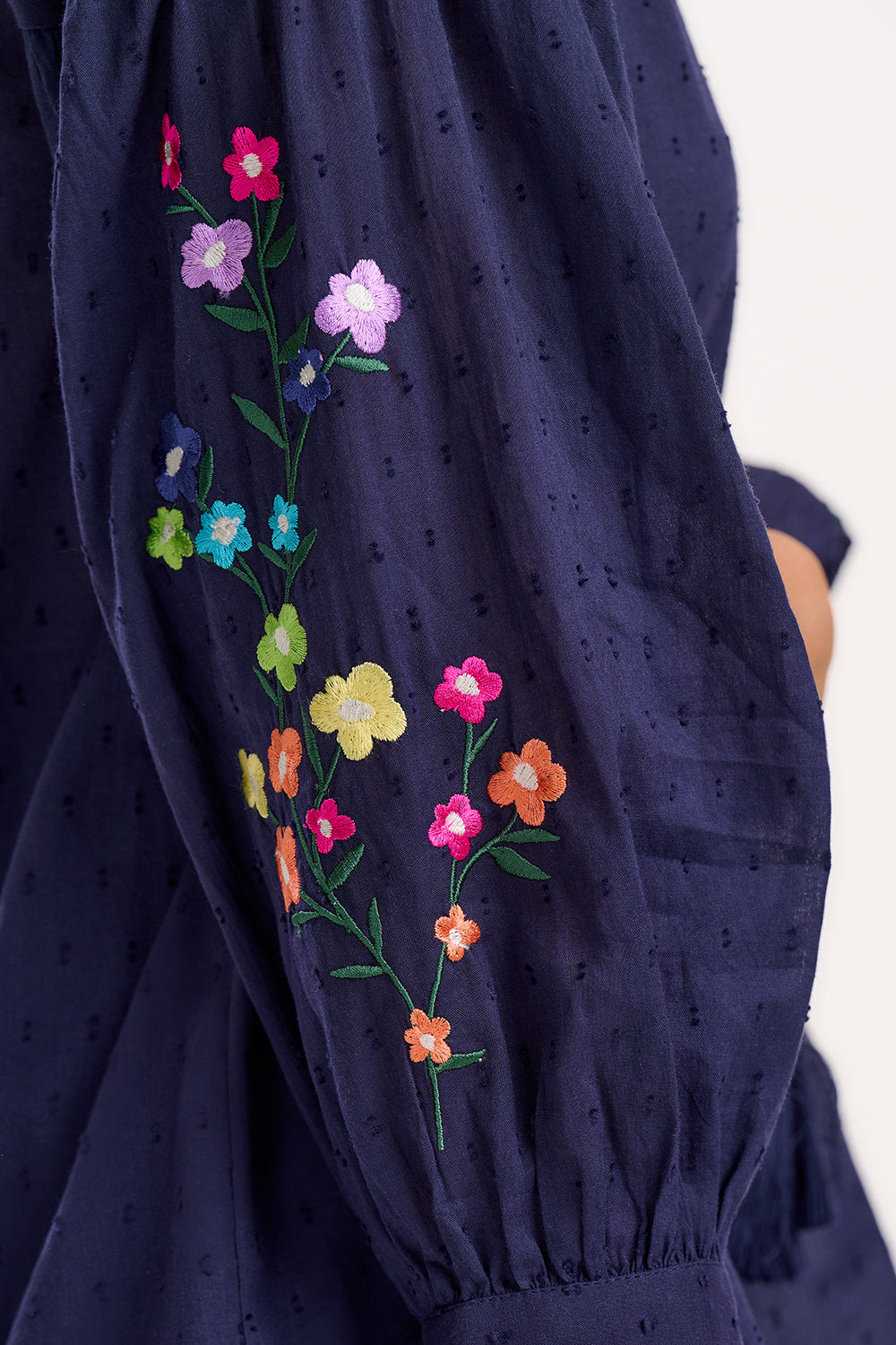 A woman wearing a navy blue boho top with embroidered flowers on the sleeves, featuring a deep V-neck with tassel ties and 3/4 length sleeves.