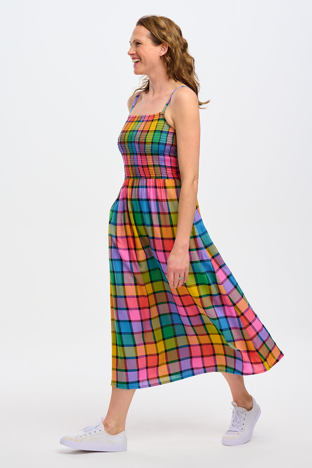 A woman wearing a multicolored checkered midi sundress with a shirred bodice and thin straps, in a rainbow check pattern.